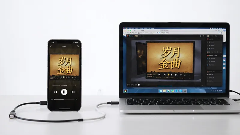 一部手机和一台笔记本电脑并排放在桌面上,手机屏幕显示“岁月金曲”播放界面,电脑屏幕显示模拟器运行同一软件的界面,画面主体是两台设备,布局左右对称,风格简洁科技感,细节有连接线暗示数据同步,画质高清,干净无多余元素