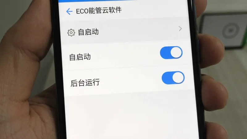ECO能管云软件在手机上的权限设置界面截图,画面中显示“自启动”和“后台运行”两个开关按钮被点亮成蓝色,背景是白色的设置菜单列表,布局是标准的安卓设置排版,风格是极简的UI设计,细节清晰,画质干净