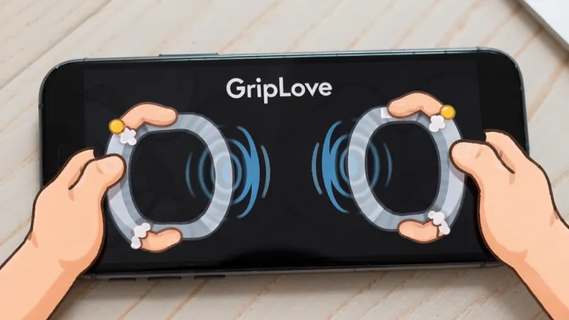 一张手机平放在桌面上，屏幕显示“GripLove”握力感应界面，画面中有两只卡通手分别握住手机左右两端，中间有动态波纹效果，背景是浅色木纹桌面，风格活泼，画质清晰，无多余元素