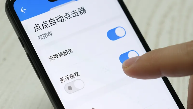 手机屏幕上显示“点点自动点击器”的权限设置页面，页面中有无障碍服务开关和悬浮窗权限开关，用户的手指正在点击开关按钮，界面风格简洁，以白色和蓝色为主，画质清晰，无多余元素
