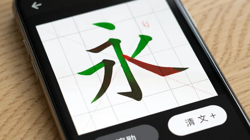 一张手机界面特写，展示练字临摹App的实时跟写反馈功能，田字格中一个“永”字，部分笔画显示为绿色表示书写正确，部分显示为红色提示调整，界面底部有清空和撤销按钮，背景是柔和的木纹桌面，风格写实清晰，画质干净无多余元素