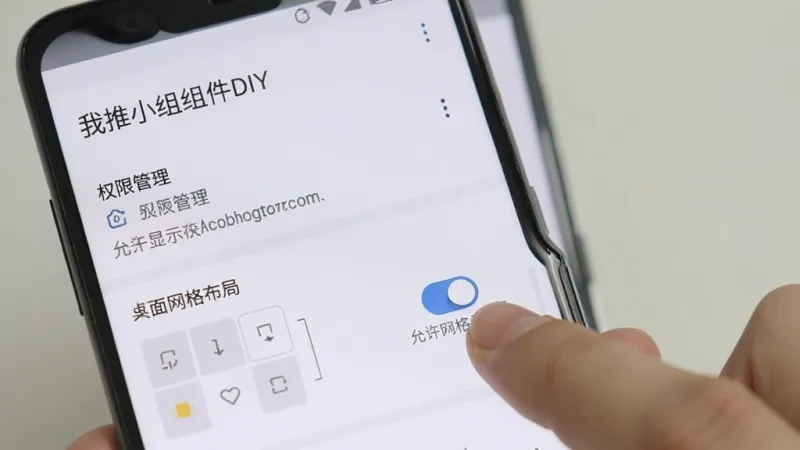 一部安卓手机屏幕显示“我推小组件DIY”的设置页面，页面中有权限管理选项和桌面网格布局选择项，画面中有一只手正点击“允许显示在其他应用上层”的开关按钮，界面风格简洁，文字清晰，画质干净，无多余元素