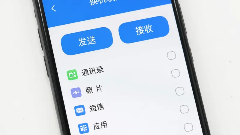 手机屏幕显示换机软件的操作界面，界面中有“发送”“接收”两个大按钮，下方有勾选列表包含通讯录、照片、短信、应用等选项，界面风格简洁明快，蓝白配色，画质干净清晰