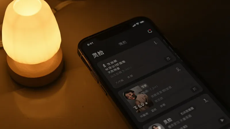 画面为“灵拾”应用暗色模式界面展示,深色背景上显示白色文字记录卡片,手机旁有一盏小夜灯,风格温馨简约,画质干净