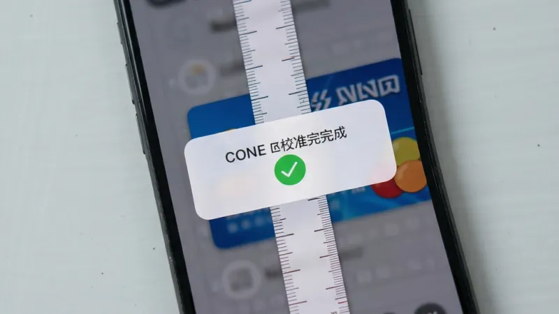 手机屏幕显示校准完成提示弹窗，虚拟尺子刻度与银行卡边缘精准对齐，界面出现绿色对勾标识，背景为浅灰色桌面，俯视角度，写实风格，画面简洁，画质清晰，无杂乱元素